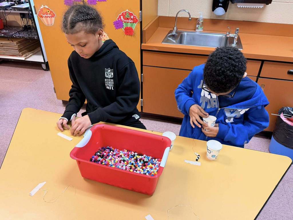 Students making a bracelet using beads and string. 