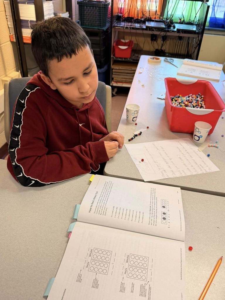 A student putting beads on a string and looking at a book. 