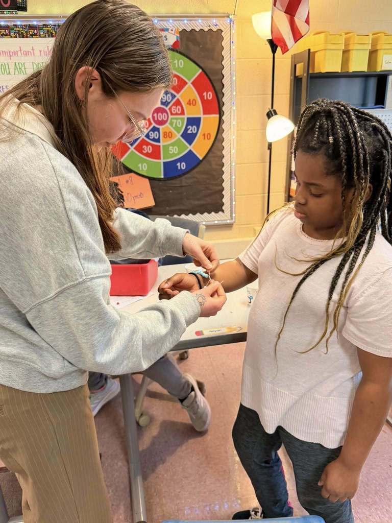 A teacher tying a beaded bracelet around the students wrist. 