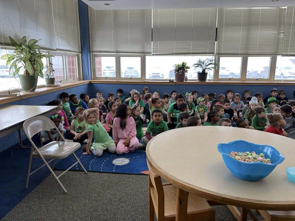 Students dressed in green for St. Patrick's Day and sitting on the floor of a library. 