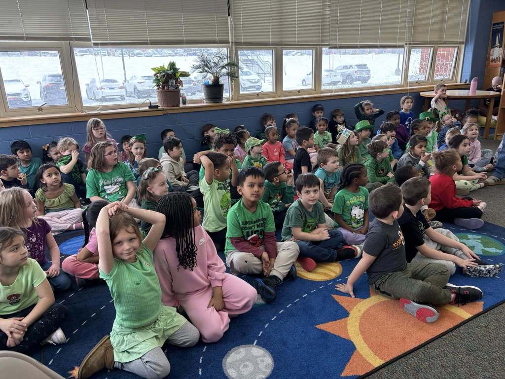 Students dressed in green for St. Patrick's Day and sitting on the floor of a library. 