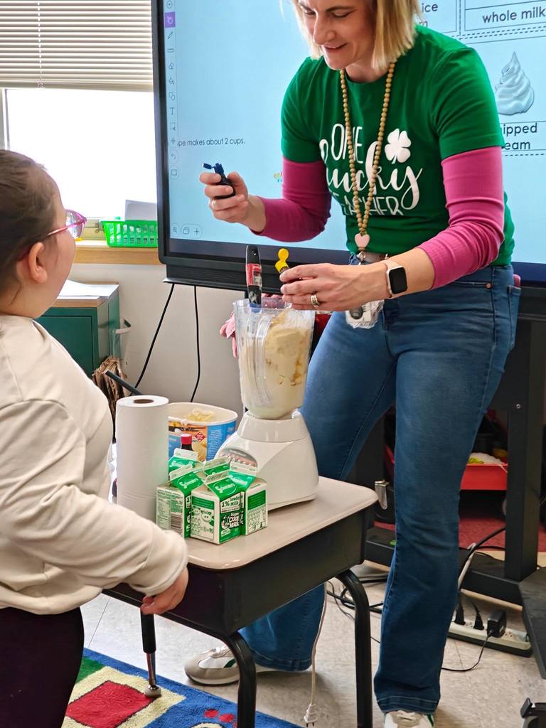 A teacher is adding food coloring into a blender. 