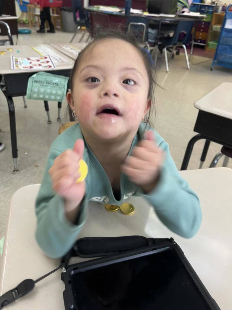 A student in a blue shirt is holding gold coin candy and smiling. 