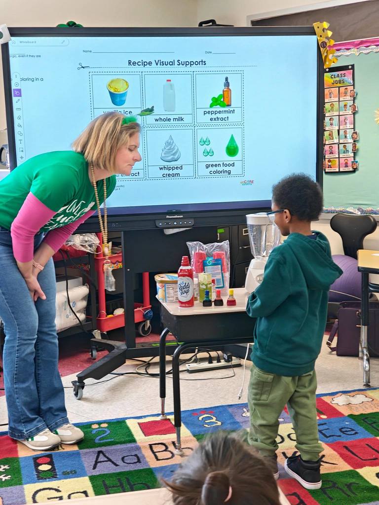 A teacher is letting a student choose what ingredient they want to add into the blender to make a shamrock shake. 