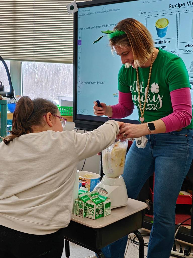 A student is helping the teacher add ingredients to a blender. 