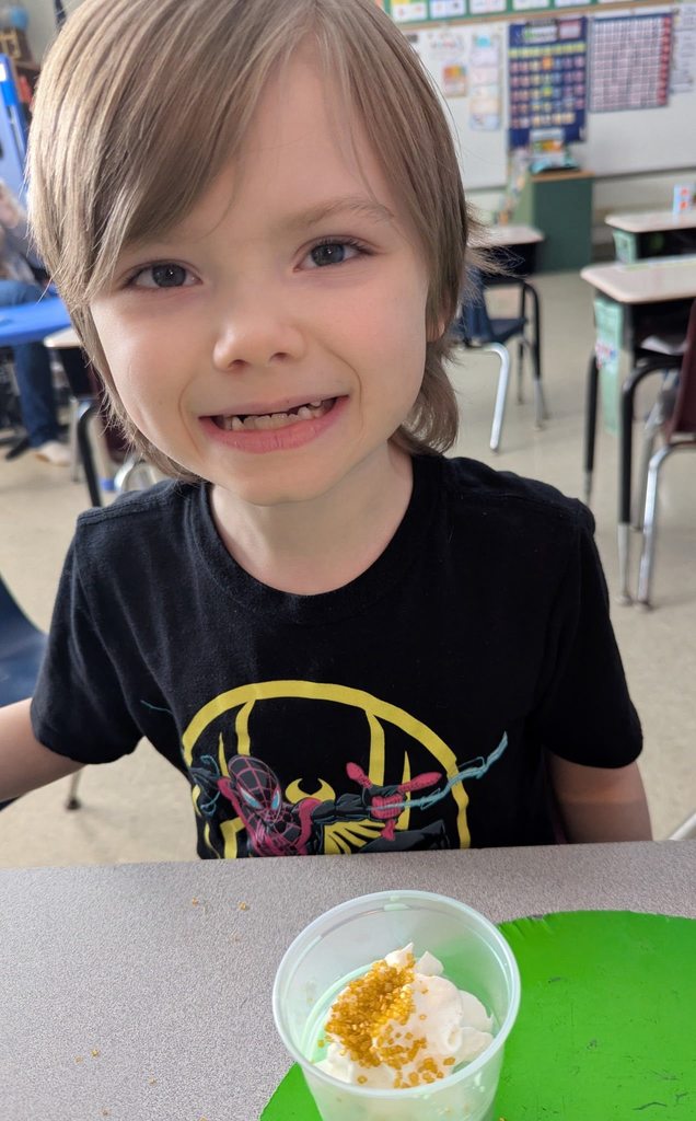 A student in a black shirt smiling with his shamrock shake in front of him. 