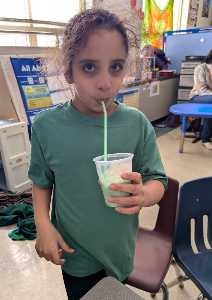 A student in a green shirt is drinking a shamrock shake they just made in class. 