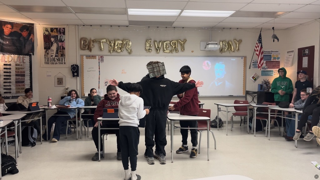 Four boys posed to recreate a scene in a short story. Classmates in desks looking on.