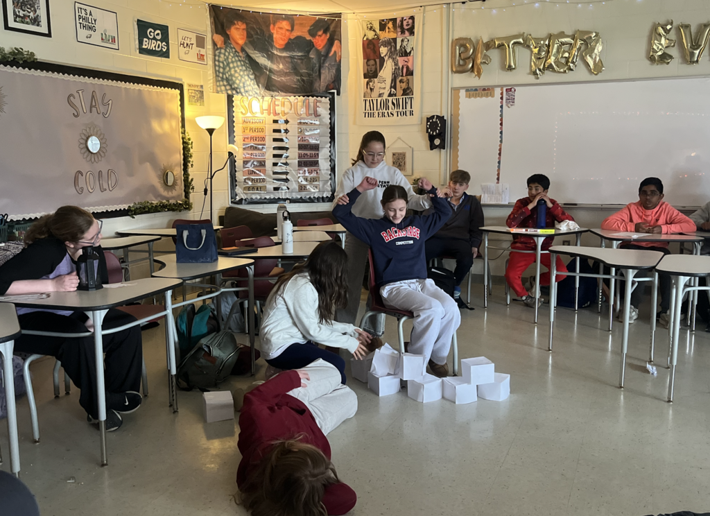 Four girls posed to recreate a scene in a short story. Classmates in desks looking on.