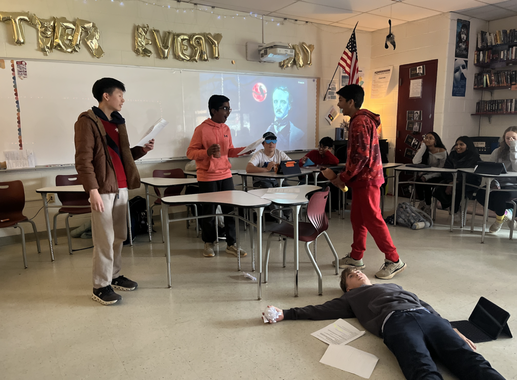 Four boys posed to recreate a scene in a short story. Classmates in desks looking on.
