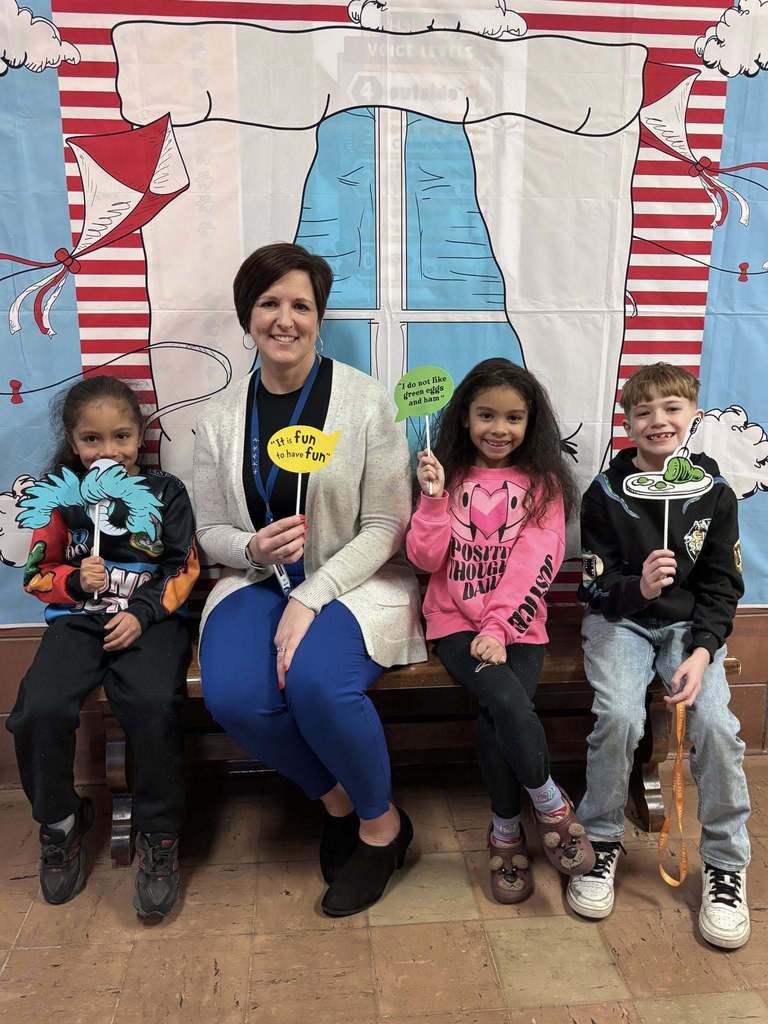 An adult and students are sitting on a bench while they hold props. 