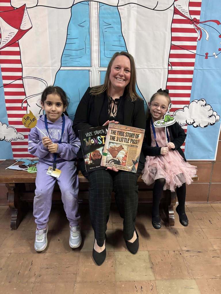 An adult and two students sitting on a bench holding a book. 