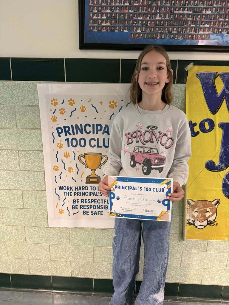 Young girl wearing a gray shirt is holding his "Principal's 100 Club" Award. 