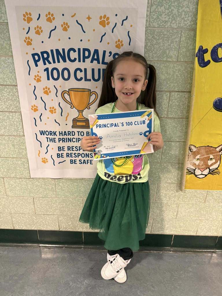 Young girl wearing green is holding his "Principal's 100 Club" Award. 