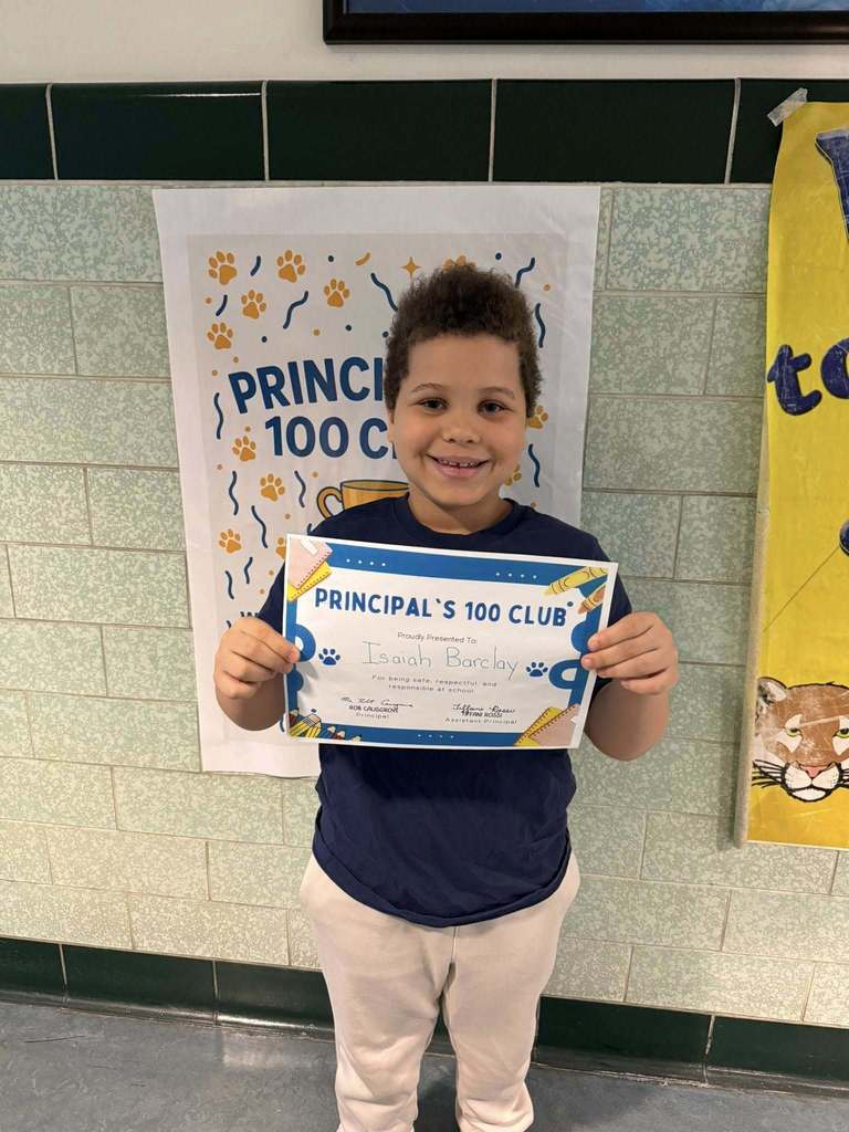 Young boy wearing a navy blue shirt is holding his "Principal's 100 Club" Award. 