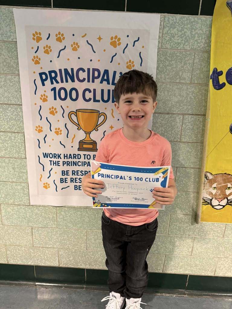 Young boy wearing a pink shirt is holding his "Principal's 100 Club" Award. 