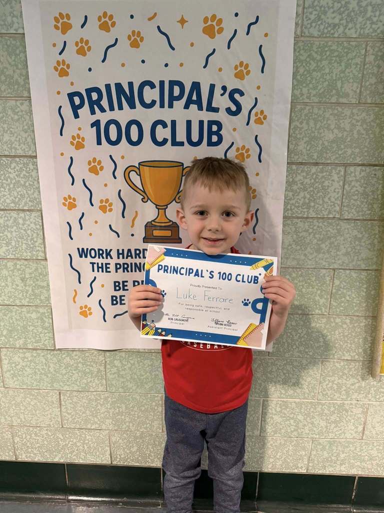 Young boy wearing a red shirt is holding his "Principal's 100 Club" Award. 