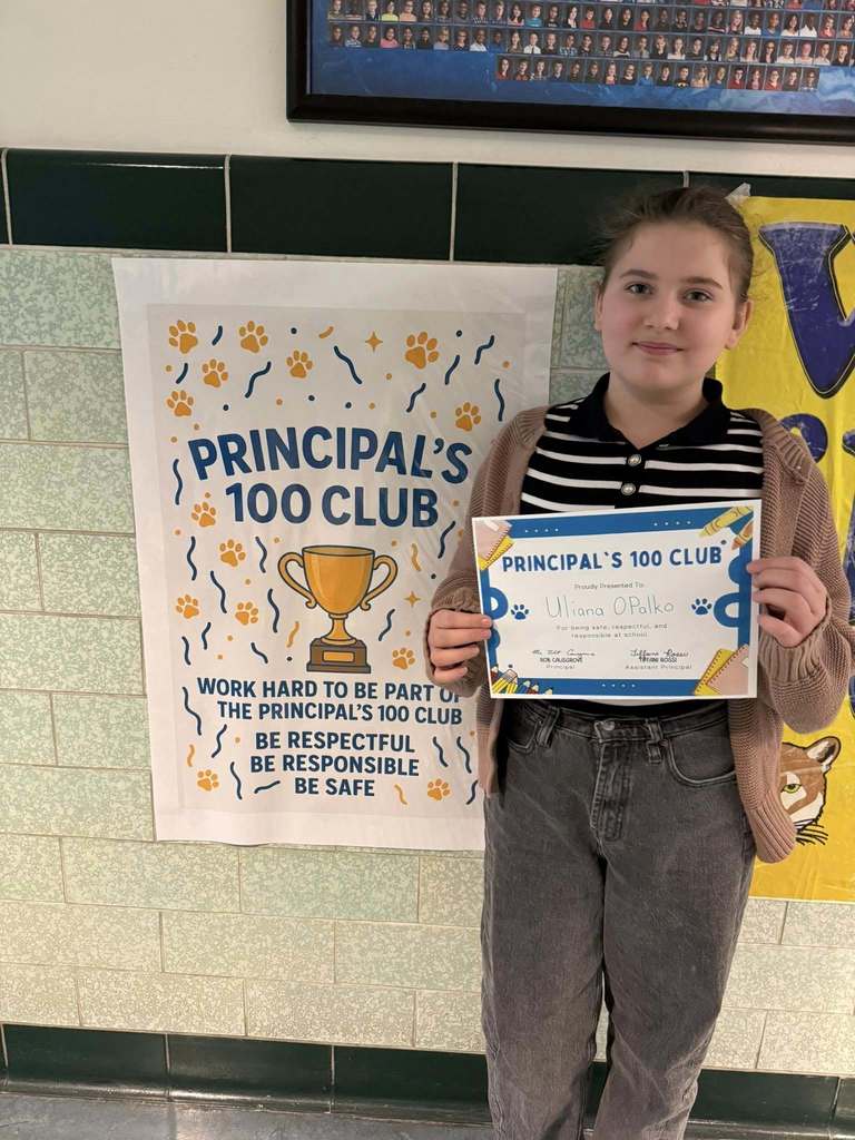 Young girl wearing a striped black and white shirt with a brown cardigan over it  is holding his "Principal's 100 Club" Award. 