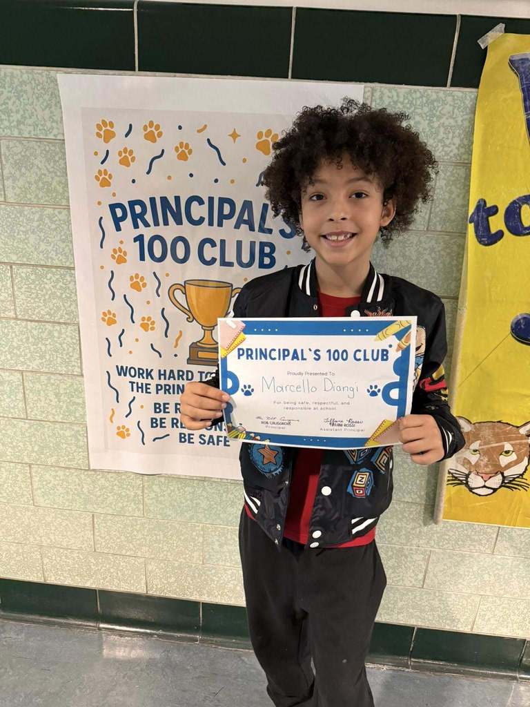 Young boy wearing a black jacket is holding his "Principal's 100 Club" Award. 