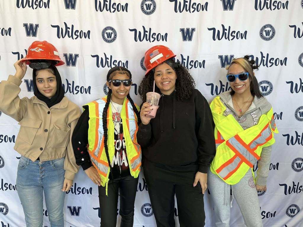 Students wearing National Duel hard hats and vests while they smile. 