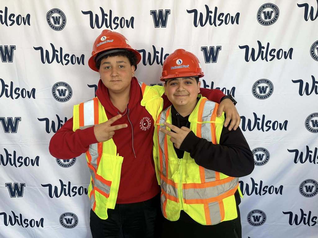 Students wearing National Fuel hard hats and vests while they smile and hold up peace signs. 