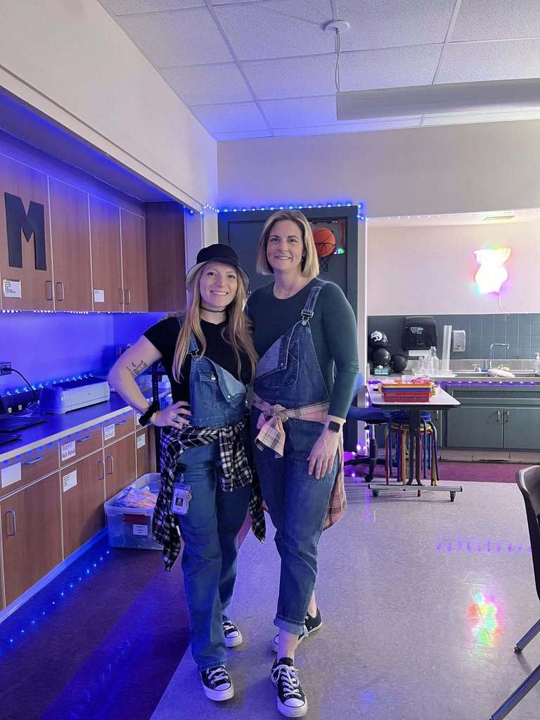Two teachers dressed in denim overall and a flannel tied around their waste for 90s day. 