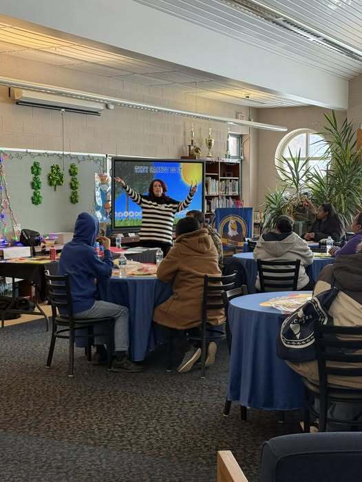 Women in a black and whites striped shirt who is from the Erie Playhouse PLAYtime is talking to students.