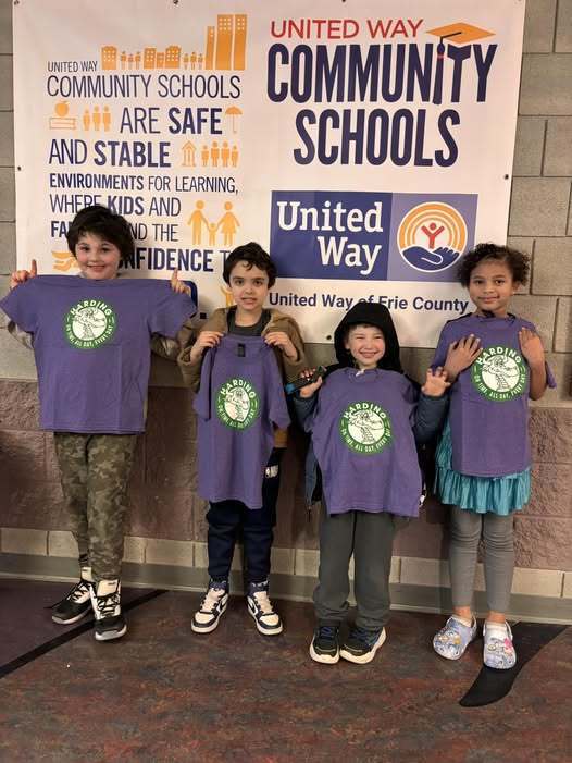 Students holding up matching purple shirts with the Harding Elementary School logo on them. 