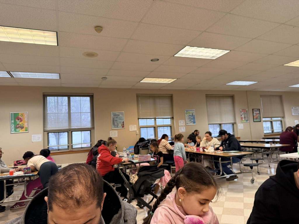 Kids and adults sitting at tables in a cafeteria and playing games.