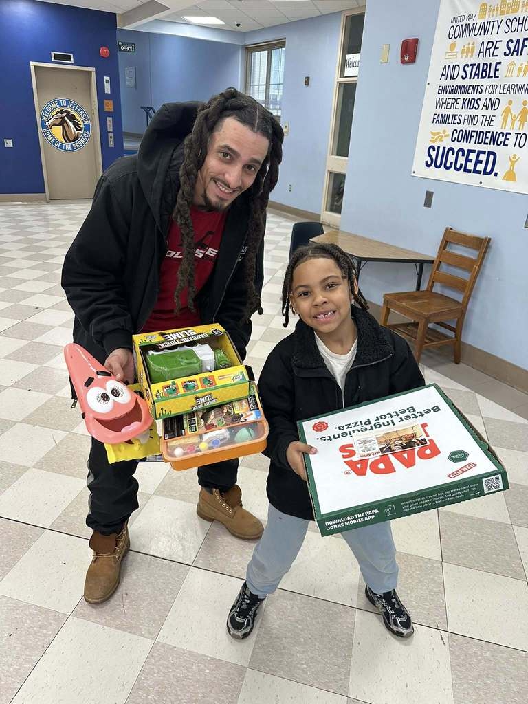 A man holding toys and games while a student holds a box of pizza. 