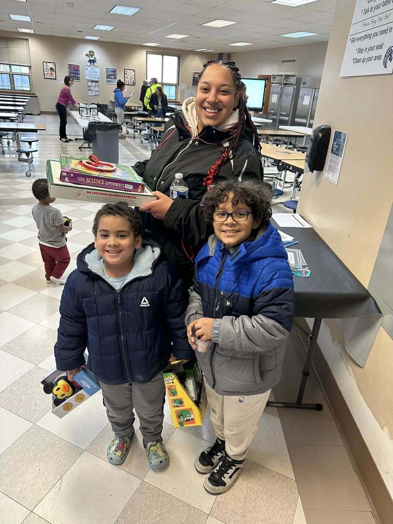 A women holding games while two students stand in front of her and are holding toys and games. 