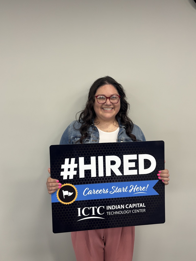 A person holding a black sign with blue and white text that says "#HIRED" in front of a white wall.