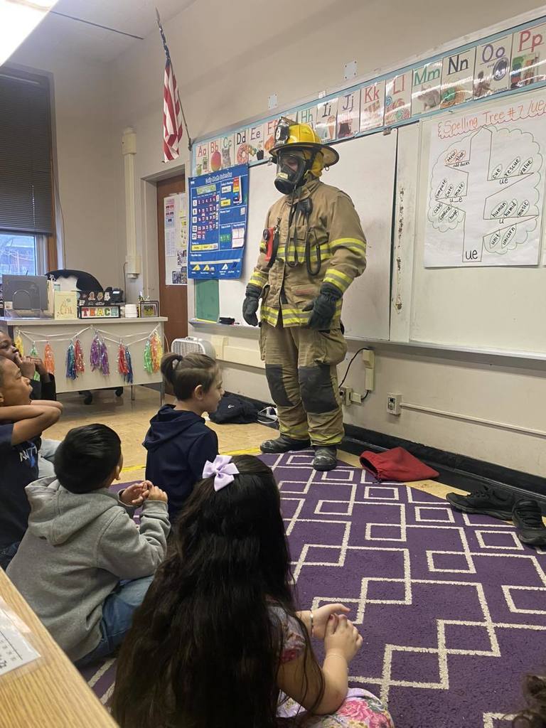 A firefighter dressed up in his gear in a classroom.