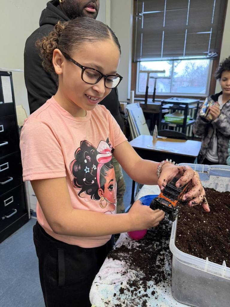 Young girl is playing with a toy car and putting dirt on it.