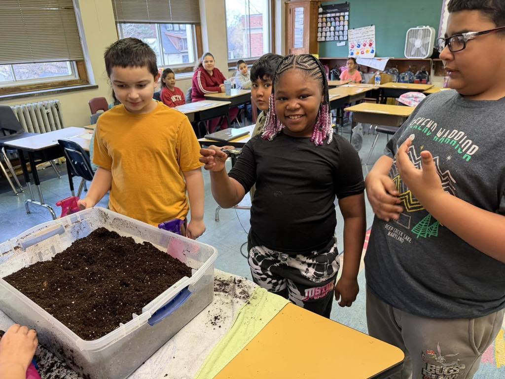 Students playing with dirt and a young girl is holding a toy car. 