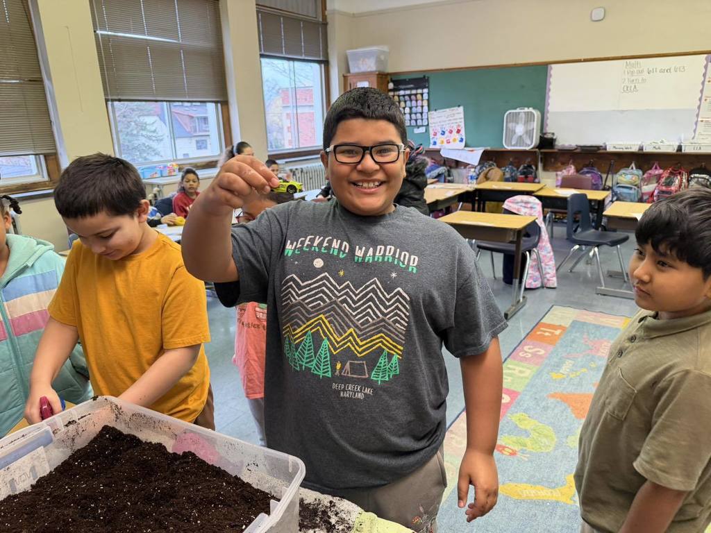 Students playing with dirt and a young boy is holding a toy car. 