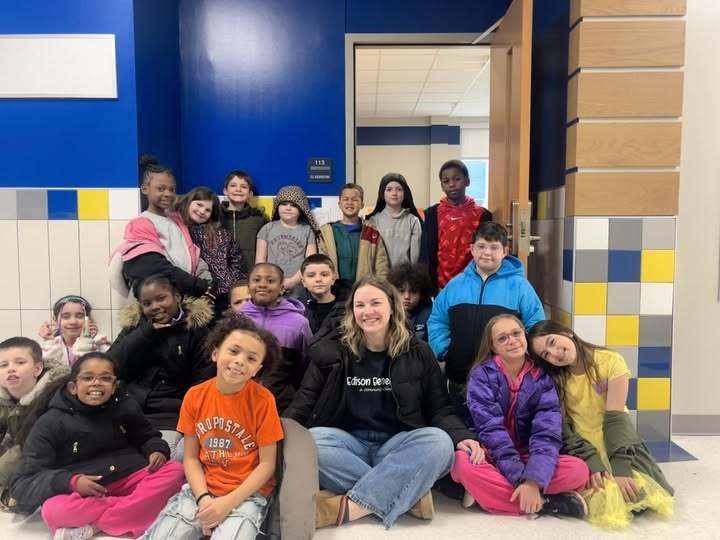 Students and a teacher sitting in the hall as a group in the New Edison Elementary School Building.