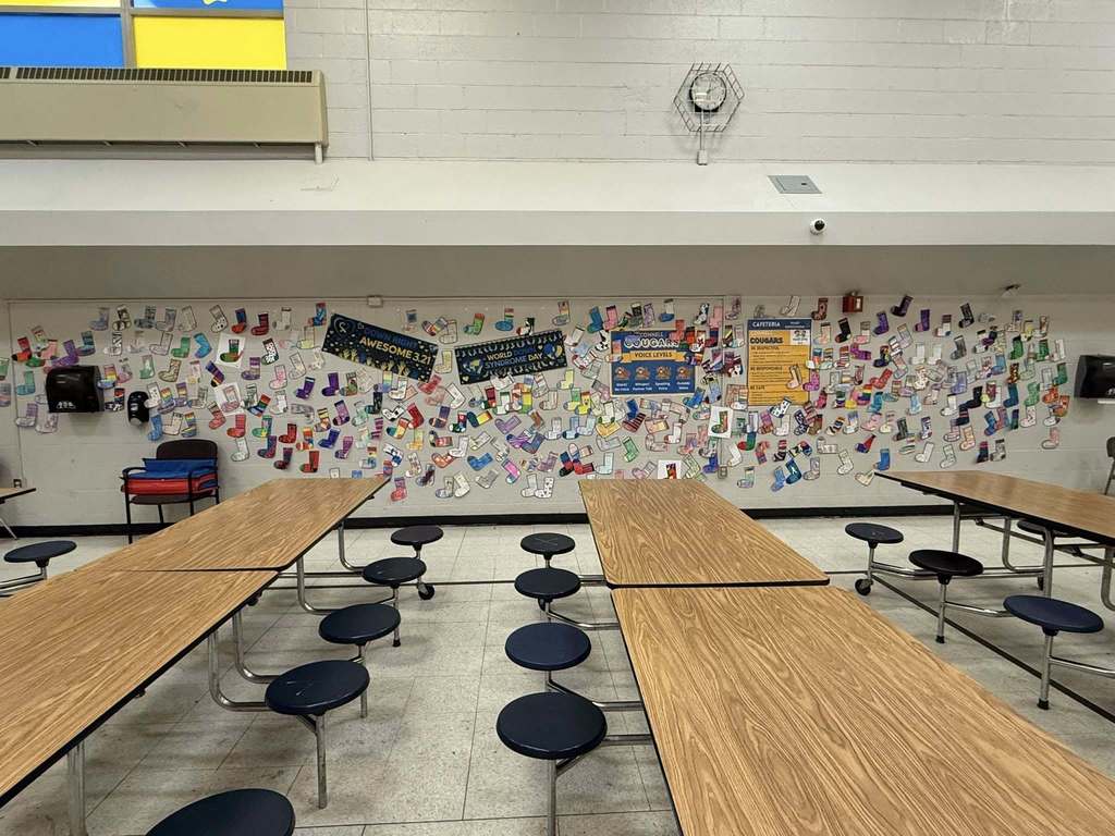 Colorful cut outs of socks that students colored are hanging on the wall in the school cafeteria. 