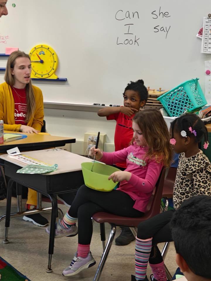 A student is mixing ingredients in a green bowl while other students watch. 