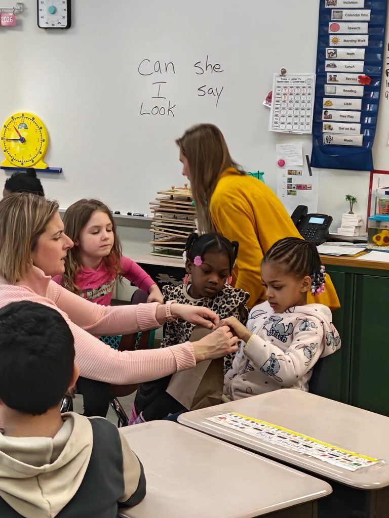 Adults helping students with a brown paper bag. 