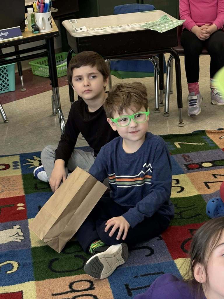 A young boy who is wearing green glasses has his hand in a brown paper bag. 