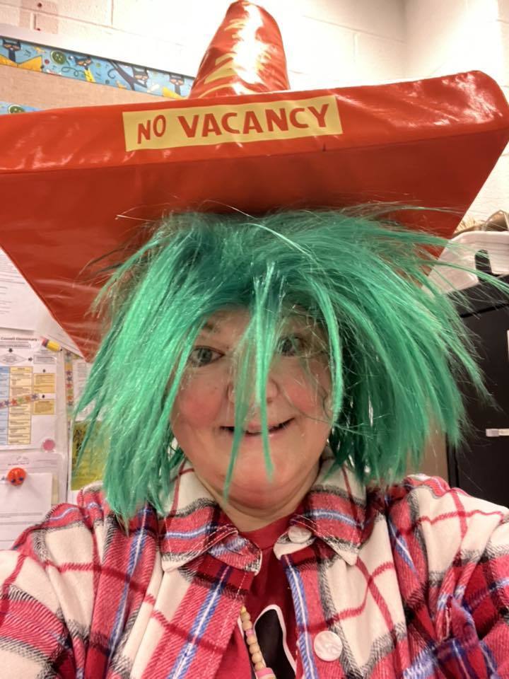 A women wearing a green wig and orange cone hat that says "No Vacancy". 