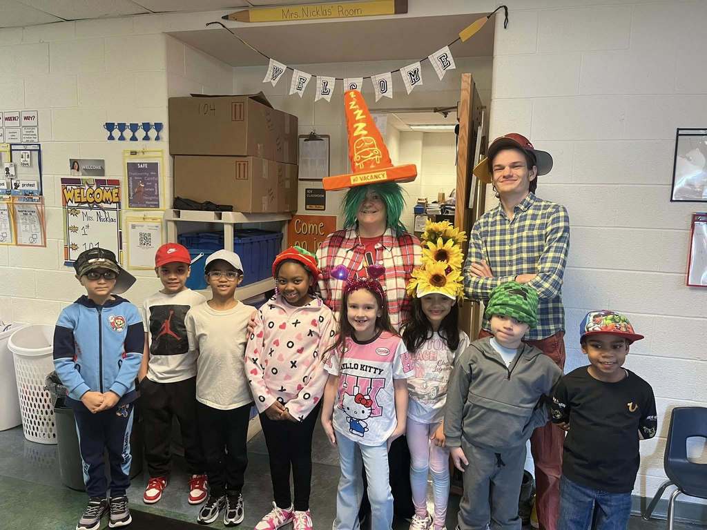 A women wearing a green wig and orange cone hat that says "No Vacancy" and students wearing different kinds of fun hats.