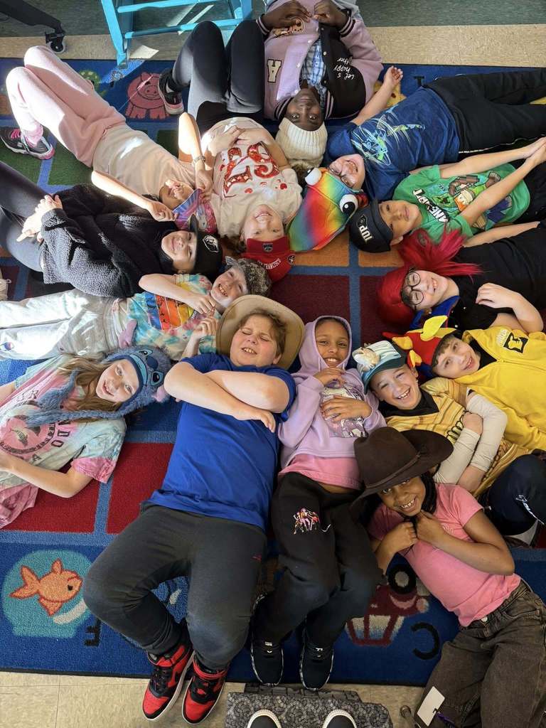 Students laying on the floor in a circle and they are wearing their fun hats. 
