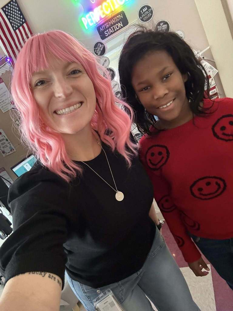 Two individuals smiling and wearing wigs. 