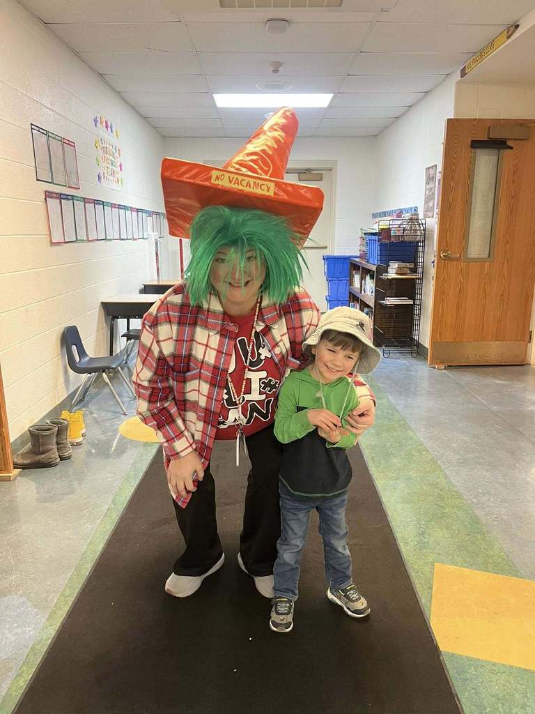 A women wearing a green wig and orange cone hat that says "No Vacancy" and a student wearing a bucket hat next to her. 