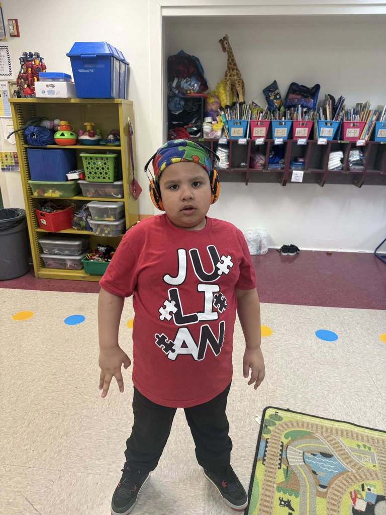 A young boy who is wearing a red shirt and a hat with puzzles on his hat, 