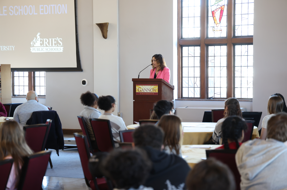 Women in a pink blazer standing at a podium and speaking.