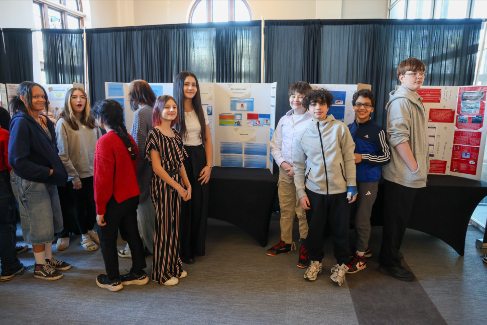 A group of students smiling in front of their projects.