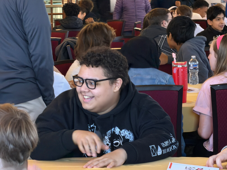 A young boy who is wearing a black hoodie and glasses is smiling. 